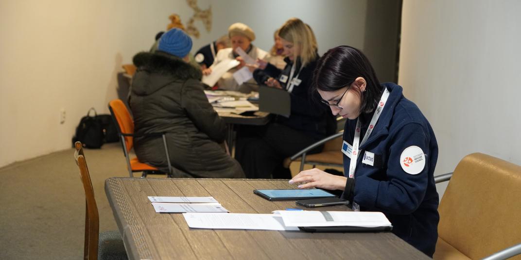 Woman sitting behind a desk with other people in the background 
